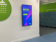 Digital display on a wall in a room with green circular sign and lockers.