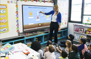 Teacher interacting with an interactive whiteboard in a classroom with students.